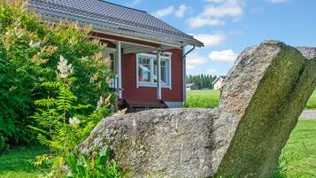 A red house with a white window and a large rock in the foreground.