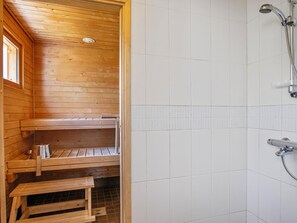 A wooden sauna with a bench and a small table, a tiled shower area, and a window. - Talvikki by Interhome (Kuopio)