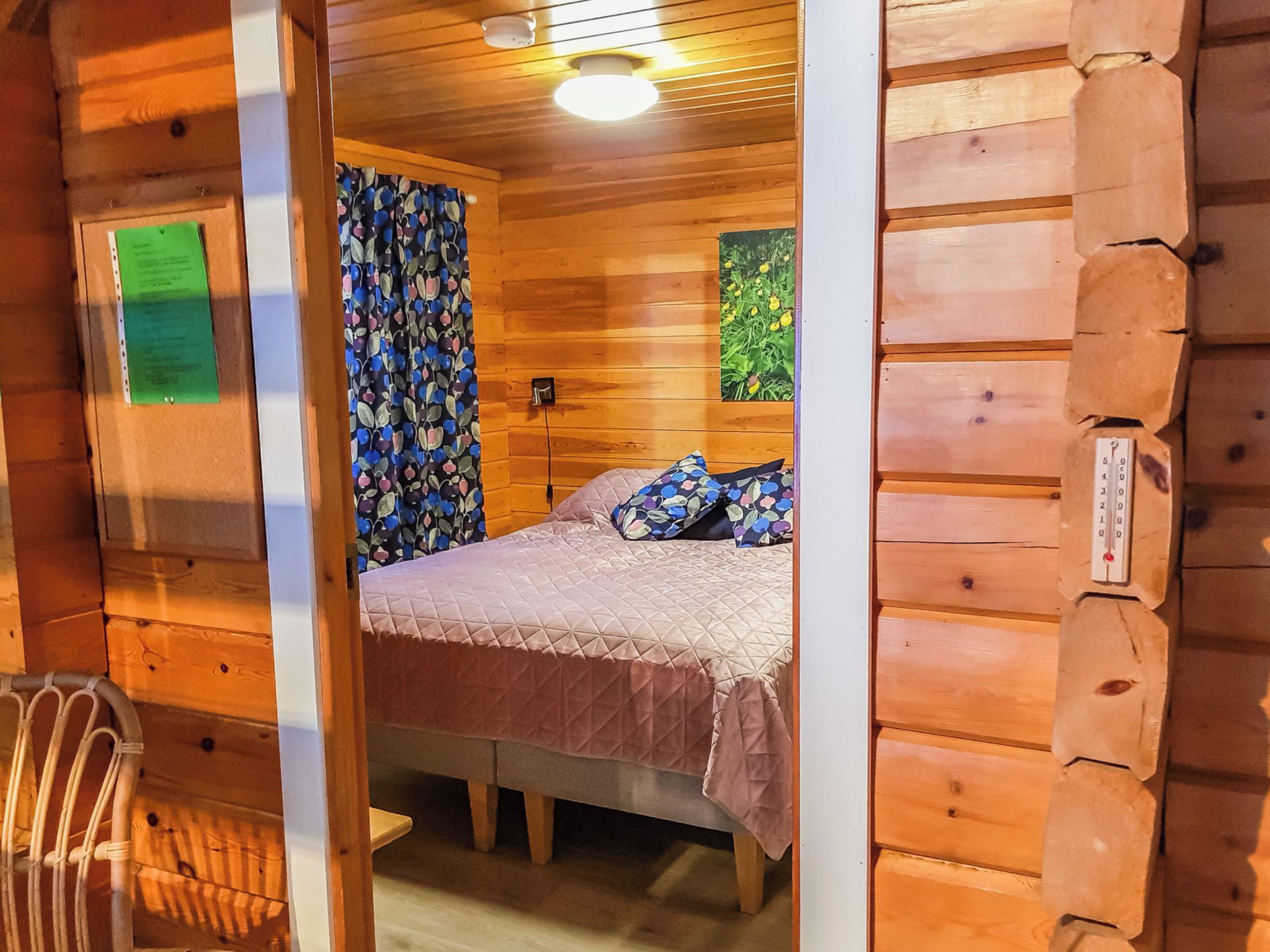 Habitación de cabaña de madera con una cama, una ventana con cortinas y un termostato en la pared.