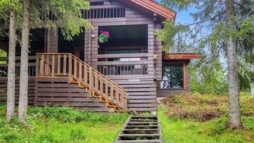 A wooden cabin with a wooden staircase leading to a porch, surrounded by greenery.