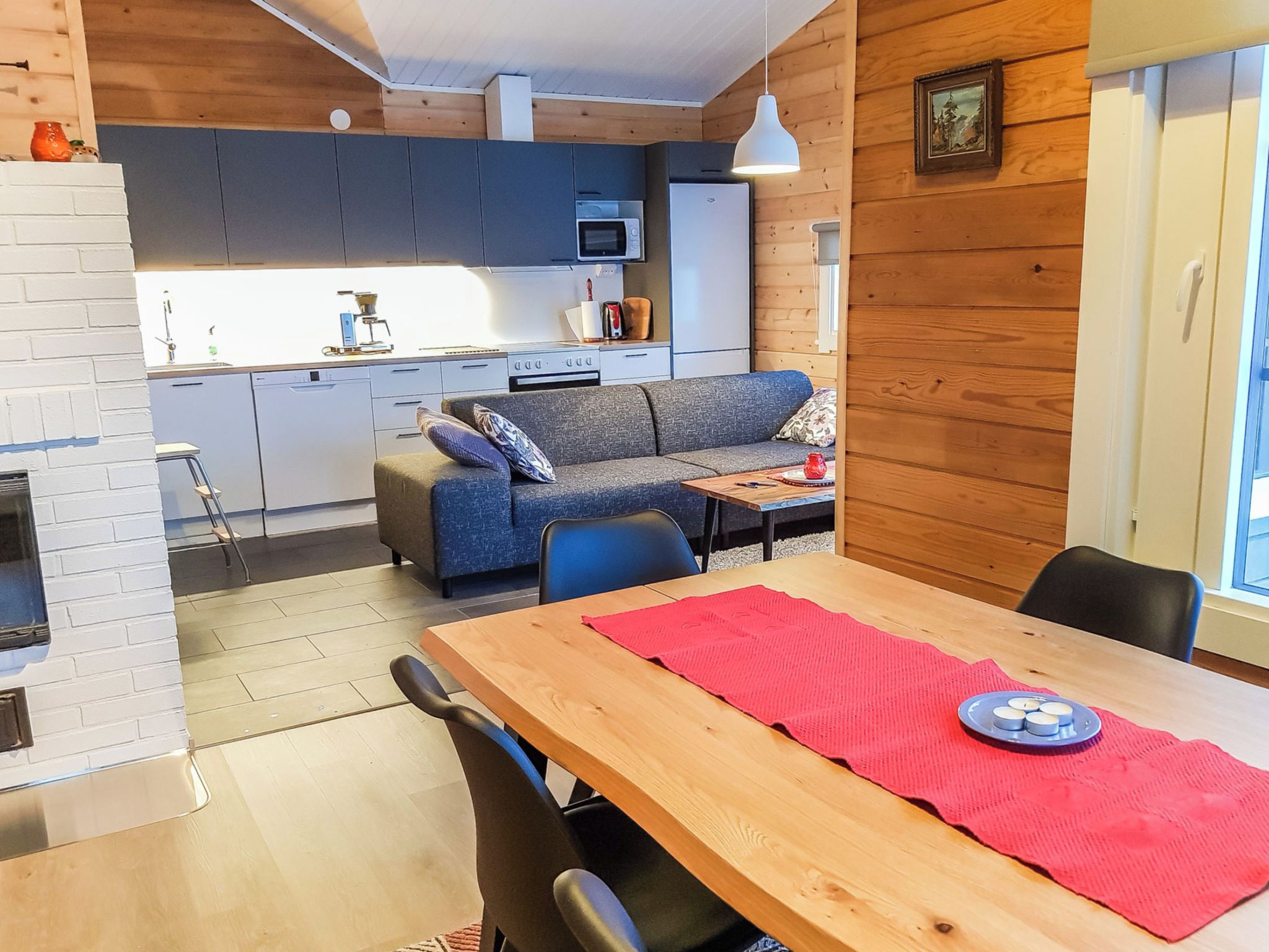 Una cocina moderna con horno y microondas integrados, una zona de comedor con mesa y sillas de madera, y un rincón de estar acogedor con sofá y cojines.
