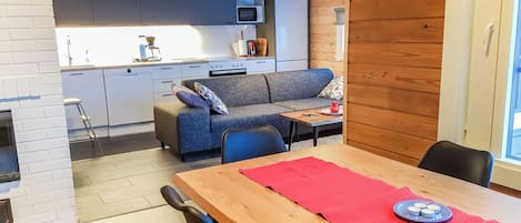 Una cucina moderna con forno integrato e microonde, zona pranzo con tavolo e sedie in legno e un angolo relax con divano e cuscini.