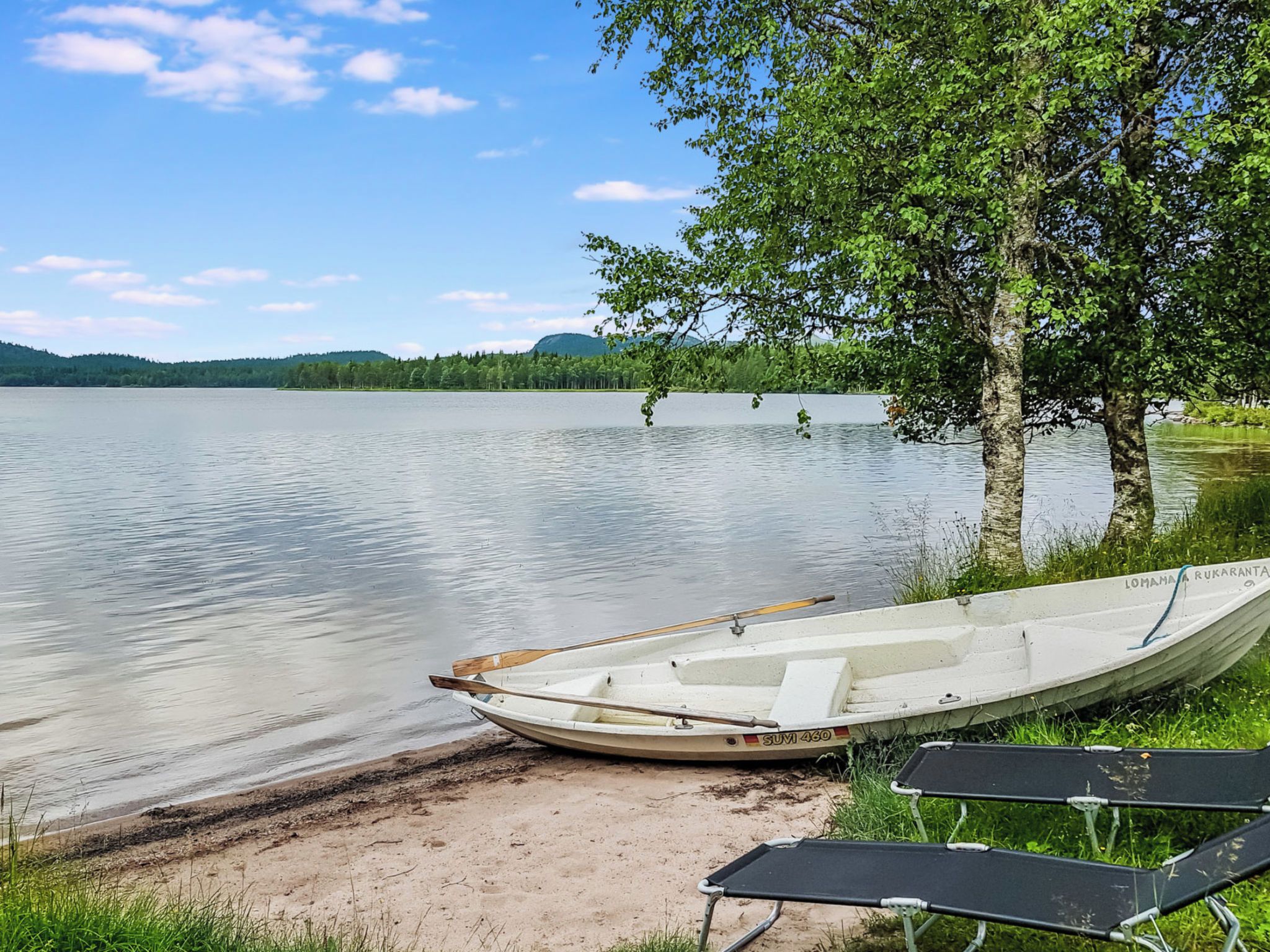 Tyyni järvi, jonka rannalla on pieni, laiturissa kiinni oleva vene. Järveä ympäröivät puut, ja taivas on kirkas.
