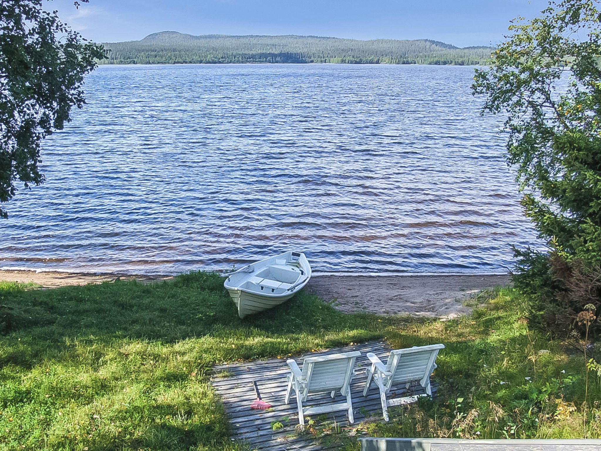 A boat on a grassy shore with a view of a lake and distant hills.