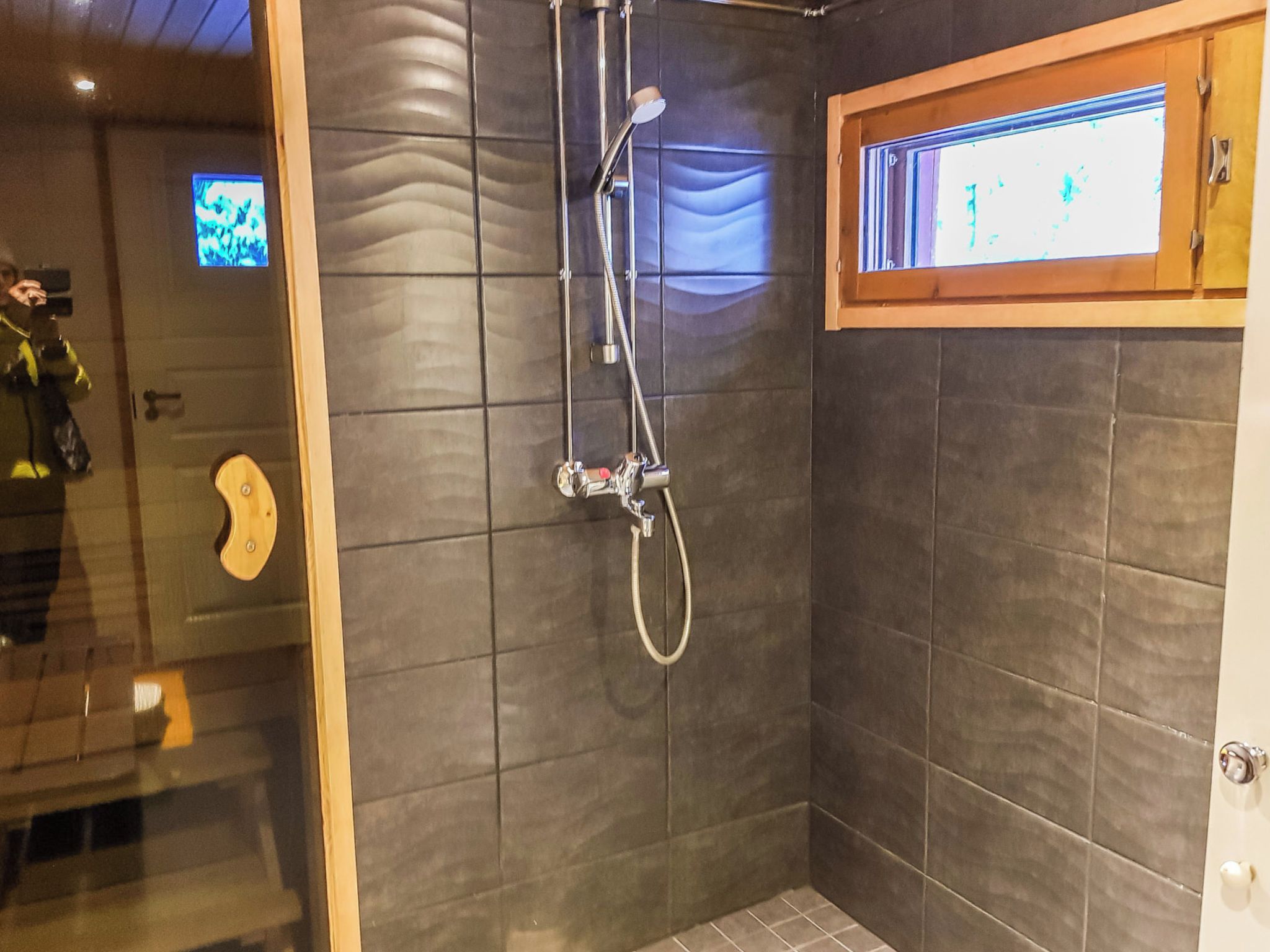 A shower area with a glass door, a wooden window, and a tiled wall.