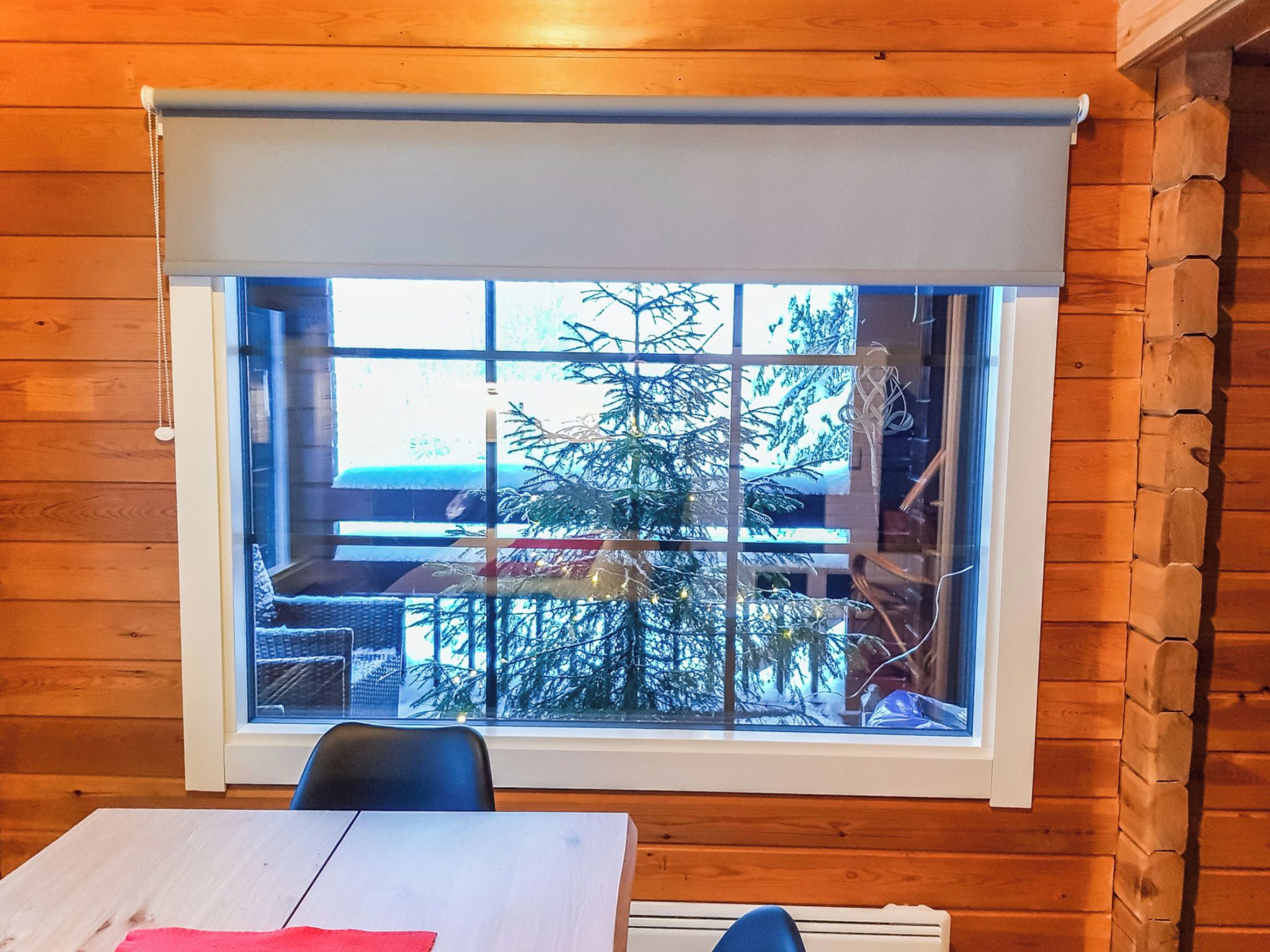 A room with a large window, wooden walls, and a table with chairs.