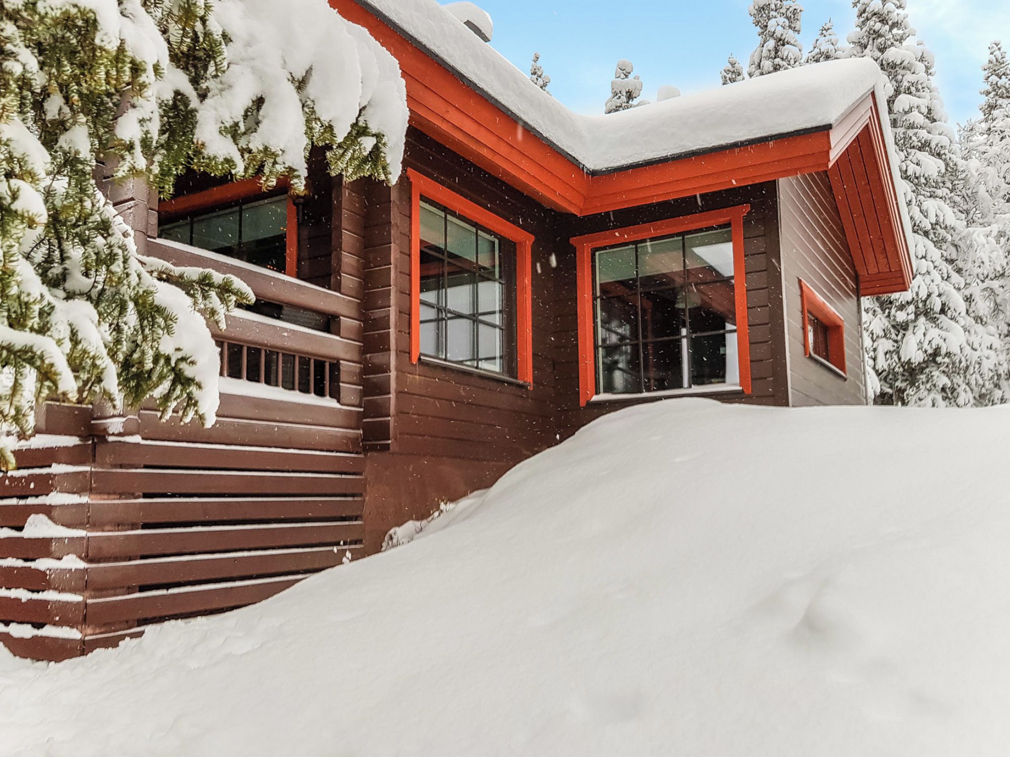 A wooden cabin with a red roof and large windows, surrounded by snow-covered trees.
