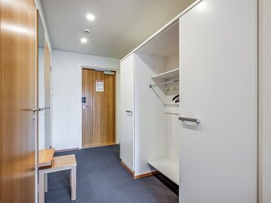 Habitación de hotel con puerta de madera, una mesita pequeña, un armario blanco y una lámpara en el techo.