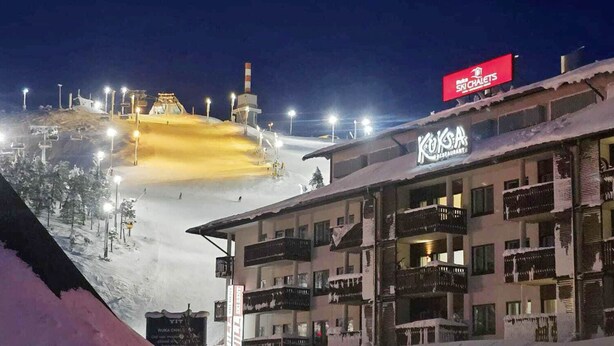 Un hôtel avec une piste de ski en arrière-plan, des télésièges illuminés et un panneau indiquant « Hill Ski Chalet ».