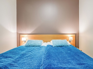 A double bed with a wooden headboard, two bedside lamps, and a blue bedspread.
