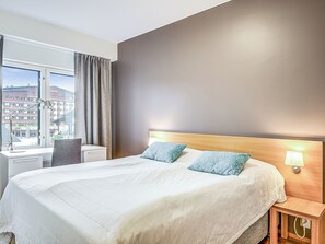 A hotel room with a large bed, a desk, and a window with curtains.