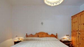 Un dormitorio con una cama de madera, dos mesitas de noche con lámparas, un armario de madera y una lámpara en el techo.