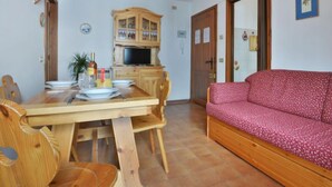 Un área de comedor con una mesa y sillas de madera, un mueble de madera con un televisor y un sofá rosa.