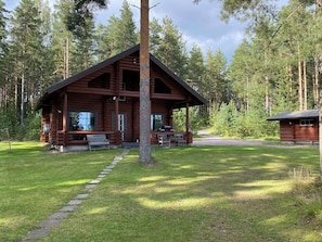 A log cabin with a porch, surrounded by a grassy area and tall trees. - Raatiannokka by Interhome (Ikaalinen)