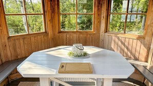 Un tavolo bianco ottagonale con un tagliere in legno e un portacandele con una candela, su un pavimento di legno con panche e un tappeto a motivi a spina di pesce.