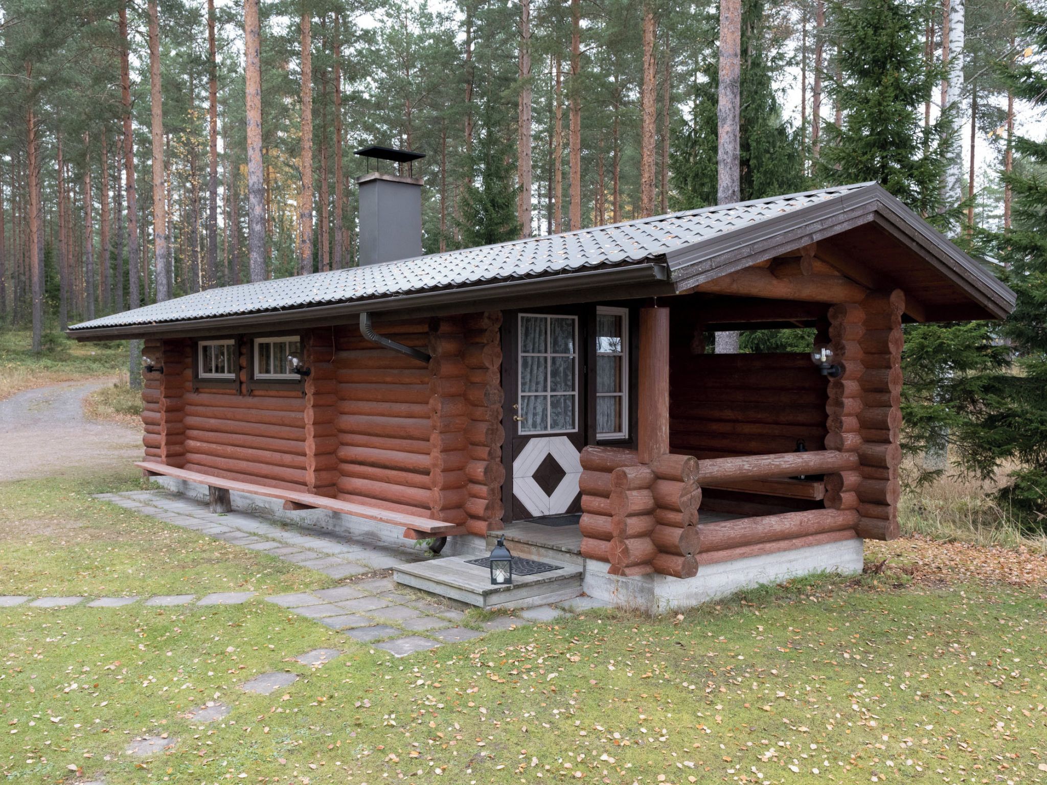 Une cabane rustique en rondins de bois, dotée d’une cheminée, d’un porche et d’une porte ornée d’une fenêtre en forme de losange.