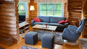 Un accogliente interno di una baita in legno con un divano, poggiapiedi, un tavolino da caffè e una lampada.