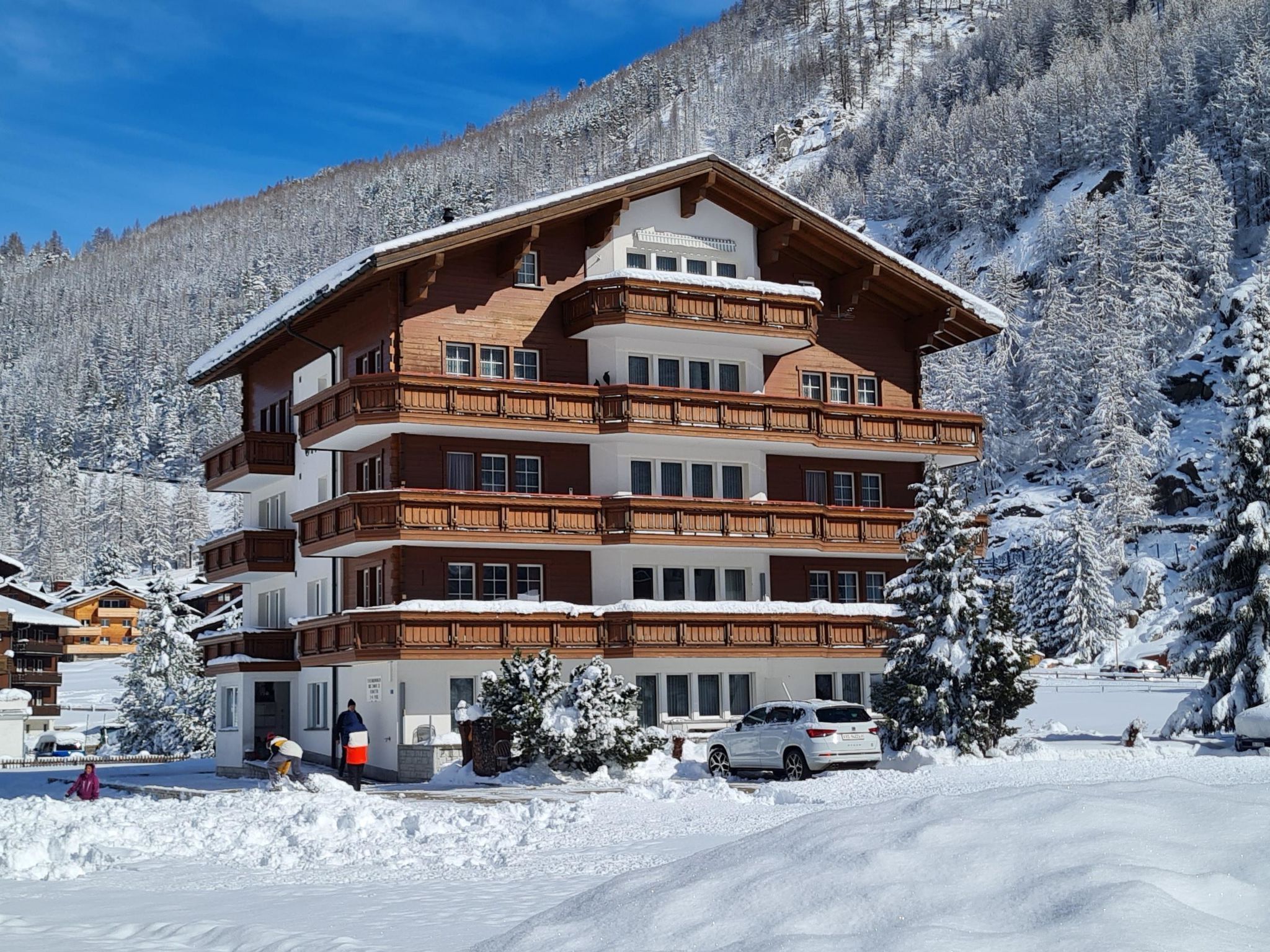 Un hotel de varios pisos con balcones de madera, rodeado de árboles nevados y montañas.