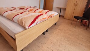 A bedroom with a wooden bed, a chair, a wardrobe, and a small table. - Apartment Orion by Interhome (Saas-Grund)
