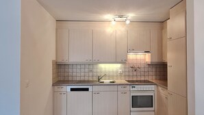 A compact kitchen with light-colored cabinets, a dishwasher, an oven, and a tiled backsplash. - Apartment Orion by Interhome (Saas-Grund)