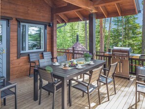 Une terrasse en bois avec une table et des chaises, un barbecue et une vue sur la forêt.