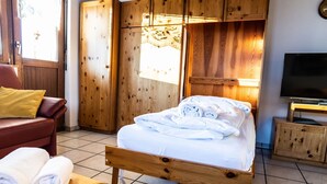 Een houten bed met witte lakens, een houten tafel met handdoeken, een houten garderobe en een televisie op een houten dressoir.