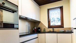 Een kleine keuken met een ingebouwde magnetron, een koffiezetapparaat en een raam met uitzicht op een besneeerd landschap.
