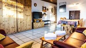 Een gezellige woonkamer met een houten tv-meubel, een eethoek met een tafel en stoelen, en een groot raam voor natuurlijk licht.