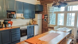 A kitchen with wooden cabinets, a stove, a dishwasher, and a dining area with a table and benches. - Piilutupa by Interhome (Luhanka)