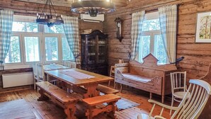 A rustic wooden cabin interior with a wooden dining table, benches, a wooden bench, a white chair, and a large clock on the wall. - Piilutupa by Interhome (Luhanka)