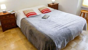 A neatly made bed with a grey blanket, two pillows with red stripes, a bedside table with a lamp, and a smartphone on the bed. - L'Univers by Interhome (Chamonix)