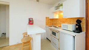 A compact kitchen with white cabinets, a microwave, a coffee maker, and a small stool. - L'Univers by Interhome (Chamonix)
