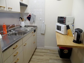 Une cuisine compacte équipée d’un évier, d’une cuisinière, d’un four à micro-ondes et d’un petit plan de travail sur lequel se trouvent une bouilloire et des ustensiles.