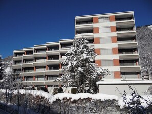 Un edificio a più piani con uno stile architettonico moderno, caratterizzato da un rivestimento in mattoni e pareti esterne bianche, e balconi ad ogni piano.