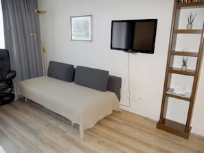 Una stanza con un letto, una televisione a muro, una sedia e uno scaffale con piante.