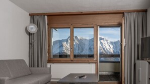 Ein modernes Wohnzimmer mit einer Couch, einem Couchtisch und Blick auf schneebedeckte Berge durch große Fenster.