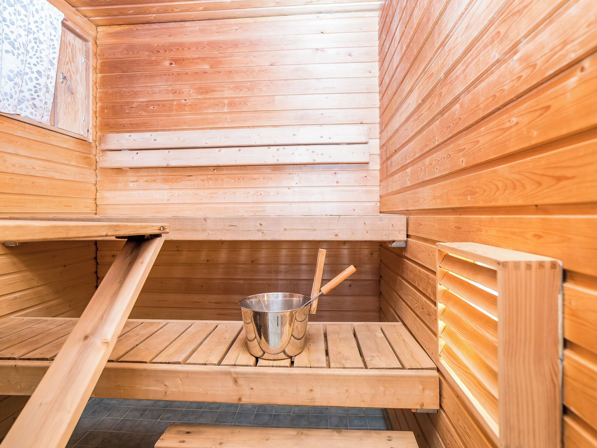 Un sauna con paredes de madera, un recipiente metálico y bancos.
