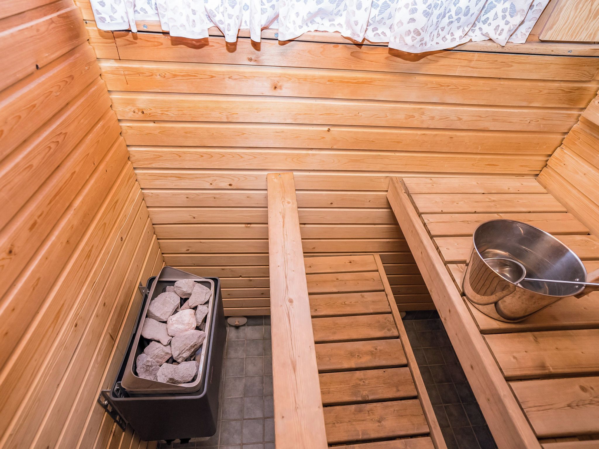Un sauna con paredes de madera, un banco, un balde de metal y un recipiente con piedras.
