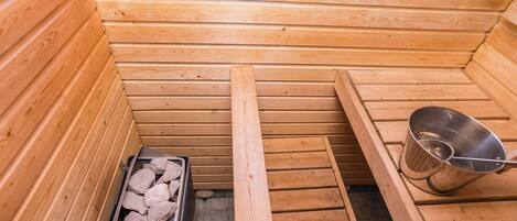 Un sauna con paredes de madera, un banco, un balde de metal y un recipiente con piedras.