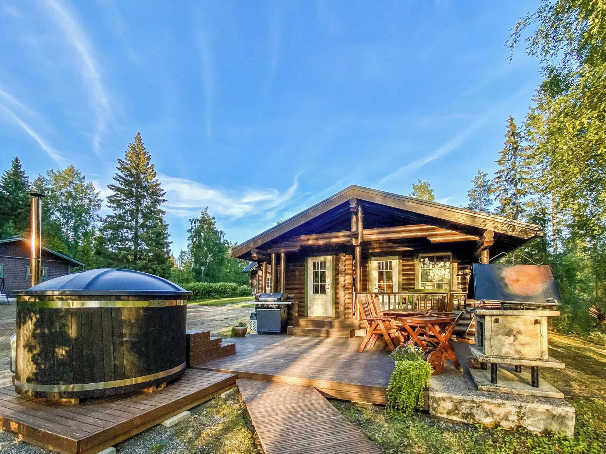 A log cabin with a porch, outdoor seating, a hot tub, and a grill area.