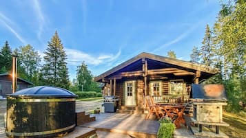 A log cabin with a porch, outdoor seating, a hot tub, and a grill area.