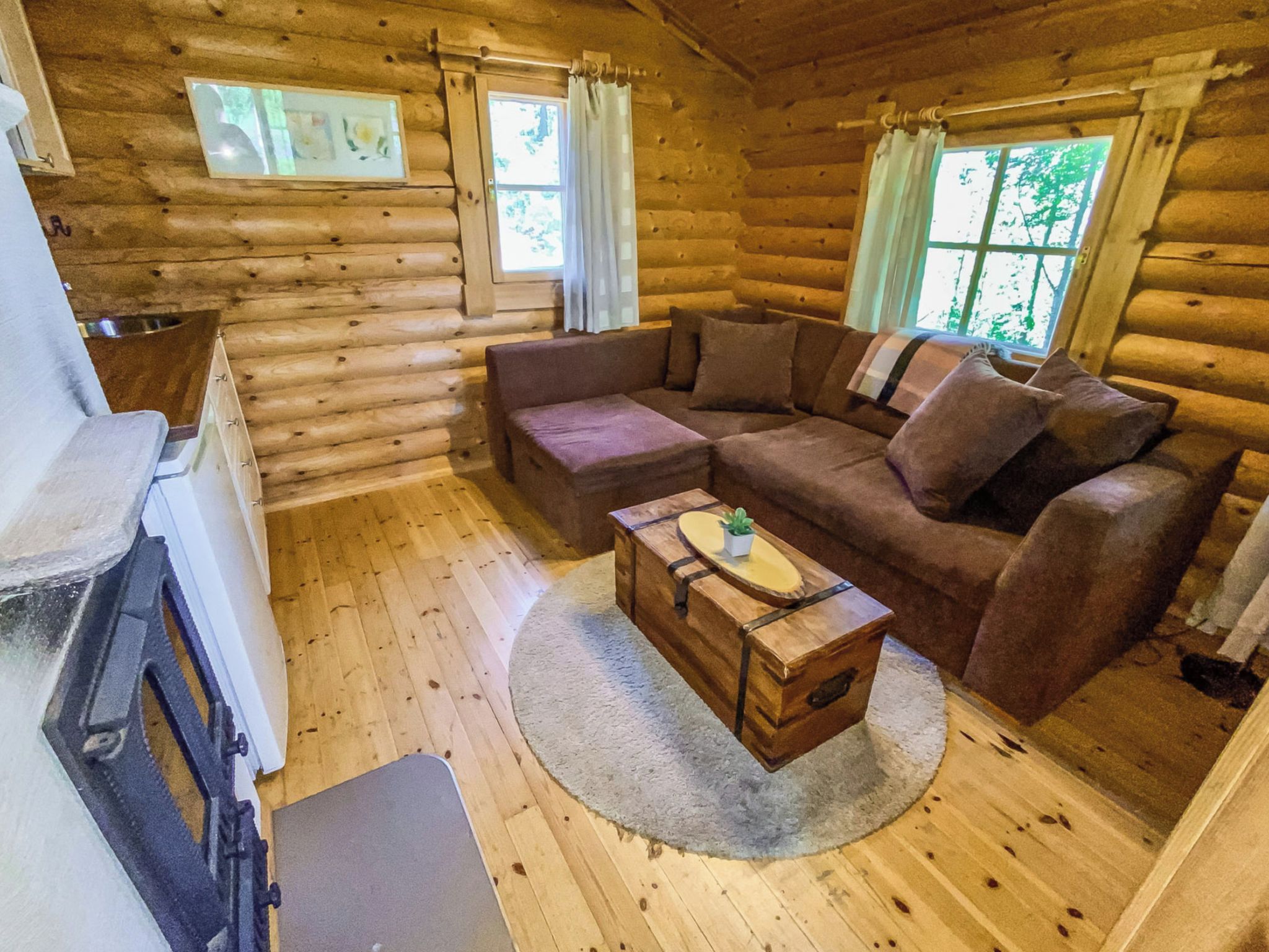 A log cabin interior with a wooden floor, a sofa, a small table with a plant, and a fireplace.