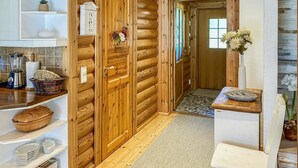 Interior de madera con una zona de cocina, que incluye estantes con vajilla y una licuadora, una cesta de mimbre y una puerta con un tirador decorativo.