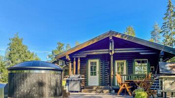 A log cabin with a porch, a grill, and a hot tub.