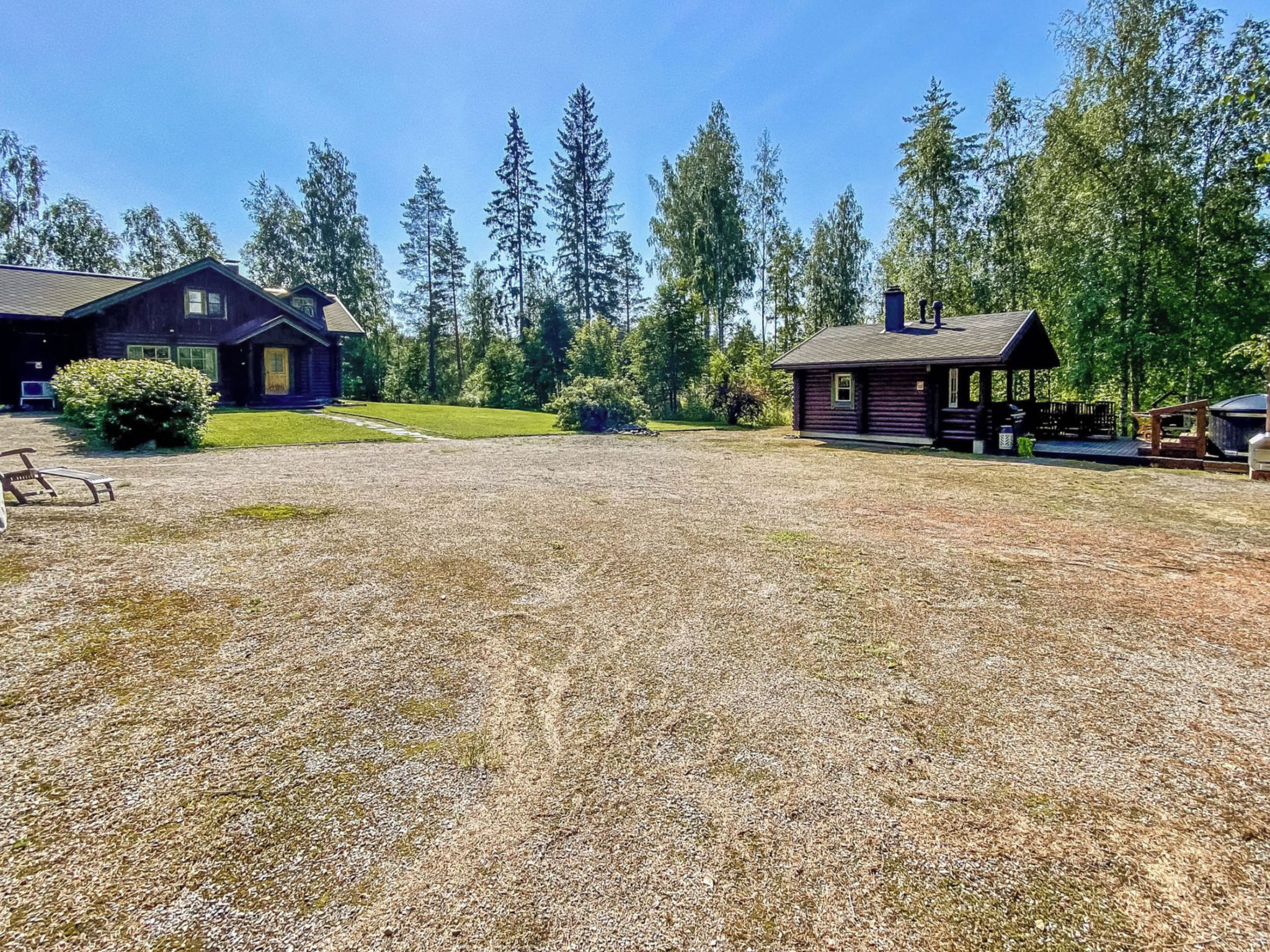 A rustic cabin with a gravel driveway, surrounded by tall trees and a clear sky.