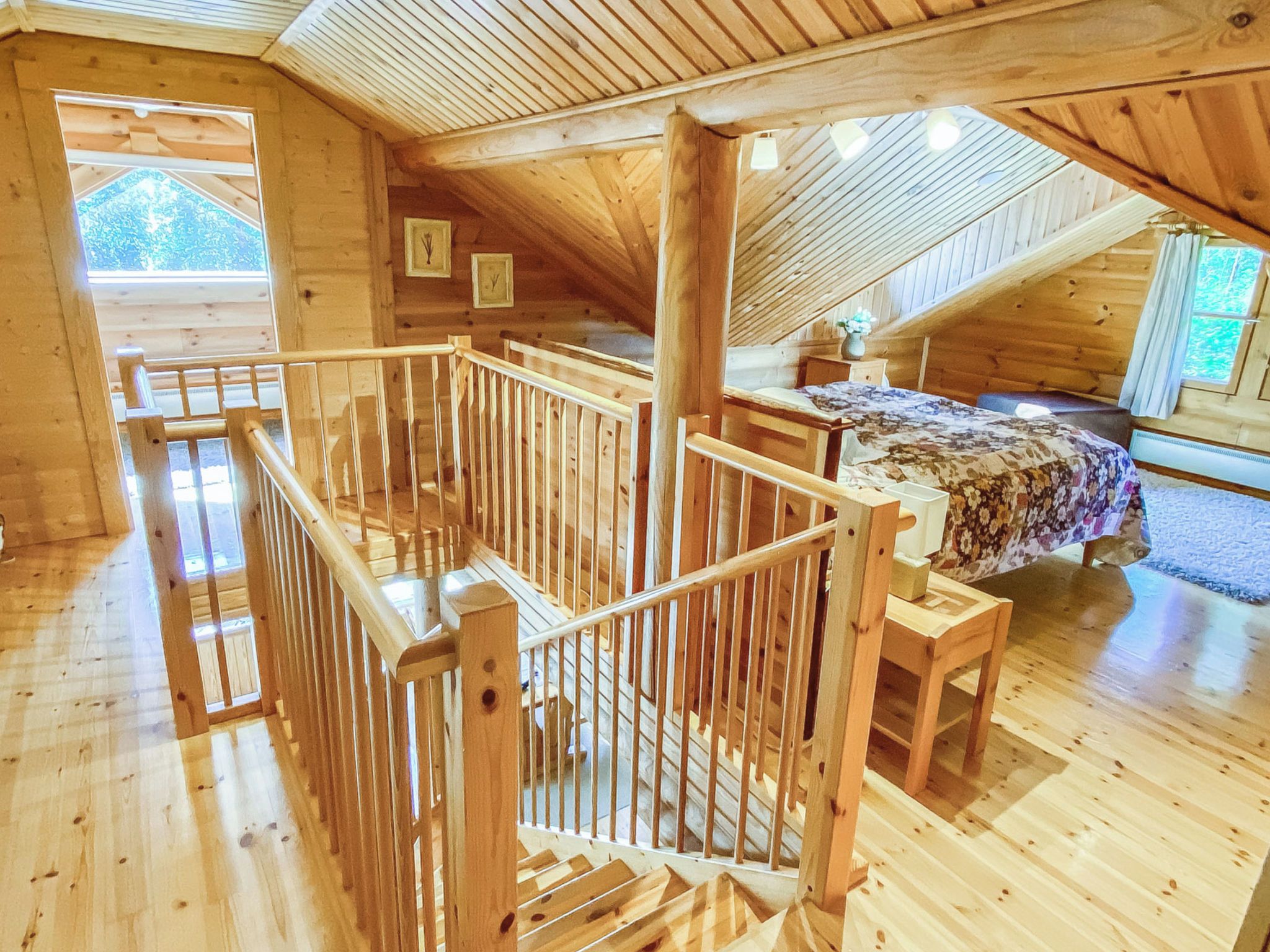 A wooden interior with a sloped ceiling, a wooden staircase, and a bed with a floral bedspread.
