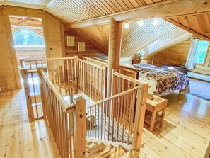 A wooden interior with a sloped ceiling, a wooden staircase, and a bed with a floral bedspread. - Hartolan ilo by Interhome (Hartola)