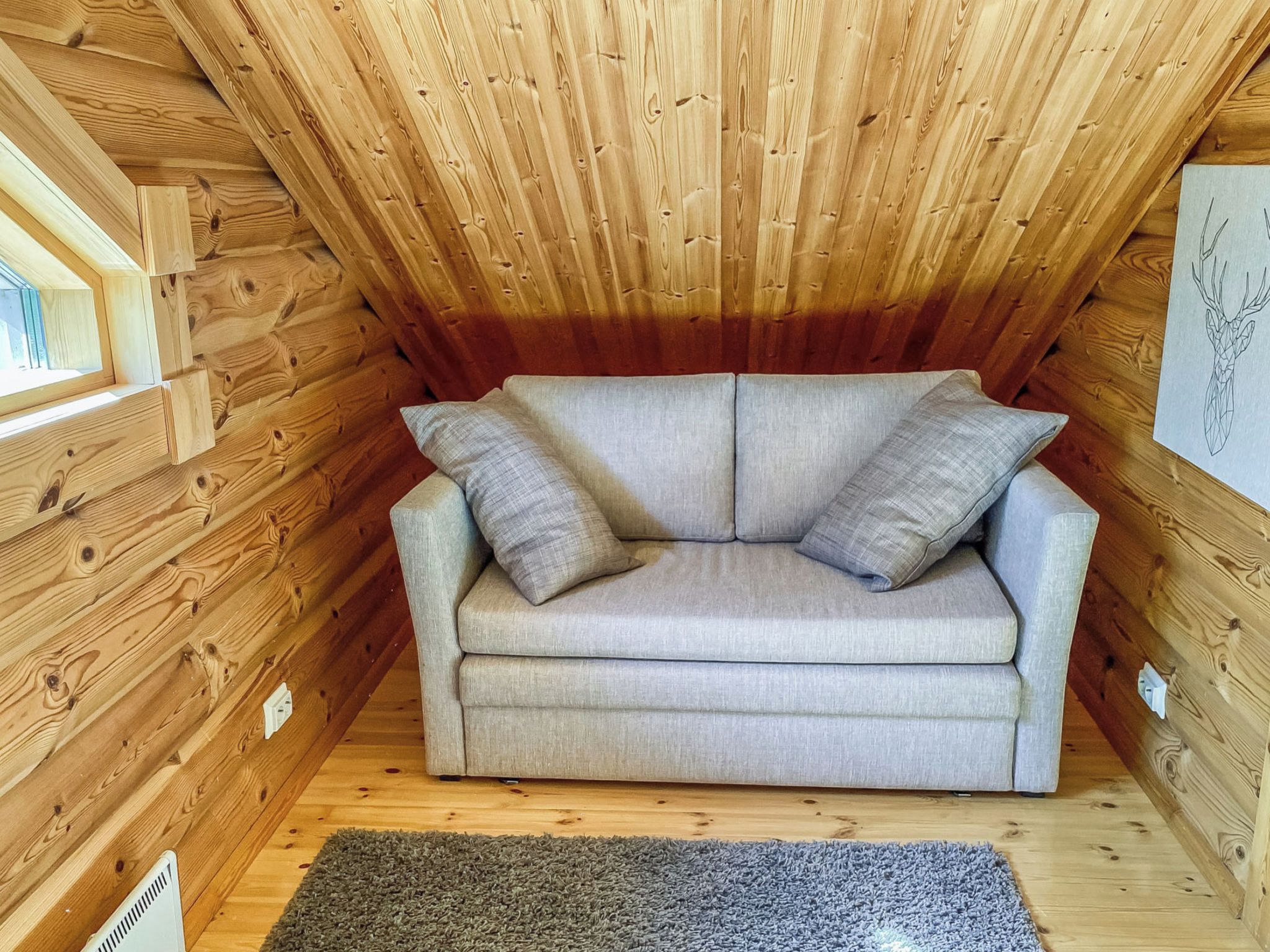 A cozy attic room with a grey sofa, wooden walls, and a small rug.