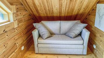 A cozy attic room with a grey sofa, wooden walls, and a small rug.