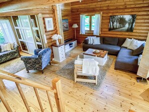 Interior de una cabaña de madera con sofá, sillón y televisor.